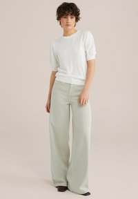Maglione bianco a maniche corte con maniche a sbuffo abbinato a jeans a gamba larga verde chiaro e scarpe scure. Tessuto liscio, design casual.