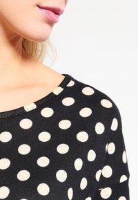 Schwarzer Pullover mit großen cremefarbenen Punkten, weitem Halsausschnitt und gerippten Abschlüssen, der eine weiche Textur und eine normale Passform bietet.