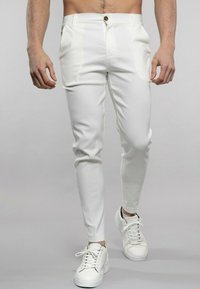 Pantalons ajustés blancs en tissu lisse, dotés d'une fermeture à bouton à l'avant et de poches en biais, associés à des baskets blanches.
