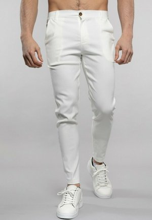 Pantalons ajustés blancs en tissu lisse, dotés d'une fermeture à bouton à l'avant et de poches en biais, associés à des baskets blanches.