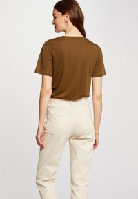 Brązowy t-shirt z krótkim rękawem i okrągłym dekoltem, w połączeniu z jasnobeżowymi spodniami o wysokim stanie z dwoma tylnymi kieszeniami i luźnym krojem.