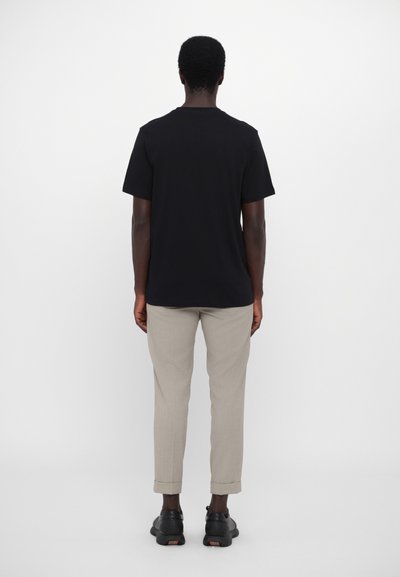 Tricou negru cu mânecă scurtă și decolteu rotund, asociat cu pantaloni bej deschis, tapered, la care se fac unghii. Încălțăminte neagră cu accente subtile.