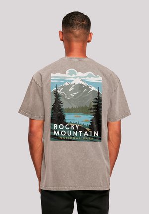 Man with short hair wearing a faded gray t-shirt featuring Rocky Mountain National Park graphic with mountains, trees, and a lake.