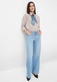Jeans a gamba larga azzurri con vita alta e due tasche laterali. Abbinati a una camicia a righe beige con bottoni e a un foulard blu a fantasia.