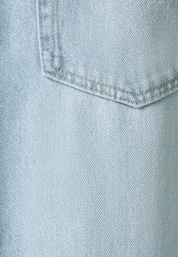 Ljusblå denimtyg med en närbild av en ficka, med synliga stygn och en något strukturerad yta.