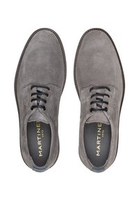Chaussures en daim gris avec des orteils ronds, des lacets noirs et des détails cousus. L'intérieur présente le logo de la marque en or. Semelle plate avec des bords texturés.