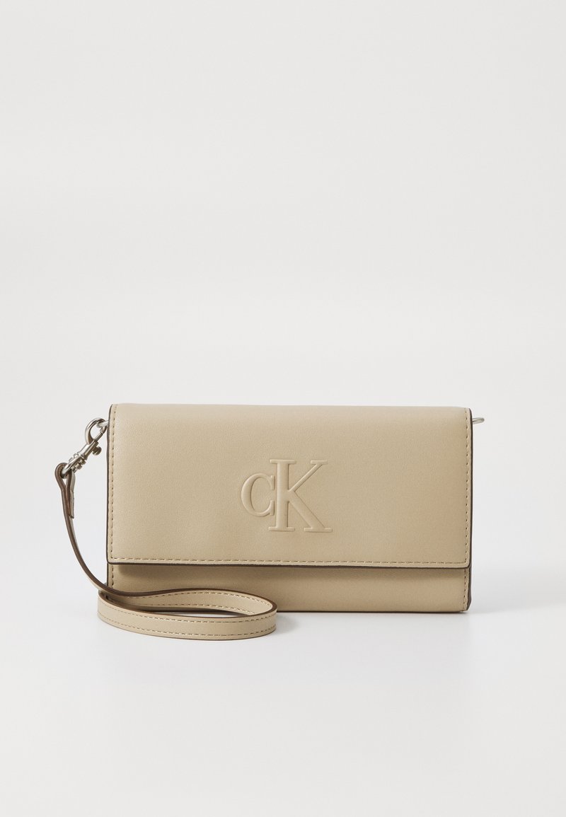 Clutch bege feito de couro liso, com logo "cK" em relevo, uma alça removível e um design dobrado.