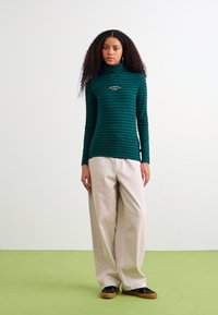 Grøn- og marineblå stribet langærmet turtleneck top lavet af blødt stof, parret med lys beige vidde bukser og sorte sko.