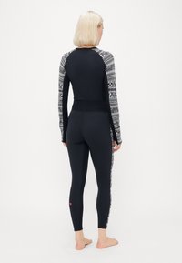 Black long-sleeve top with patterned sleeves and matching black leggings. Features a fitted design and ribbed waist, with pink logo detail.