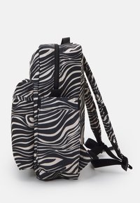 Svart och beige randig ryggsäck med rektangulär form, flera fickor, justerbara remmar och en texturerad yta.