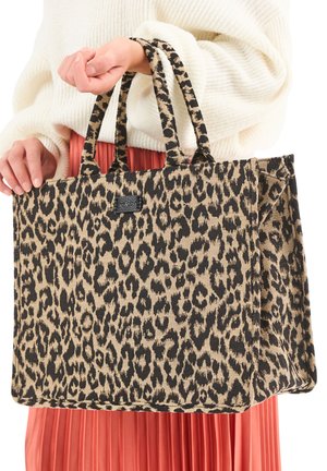 Person holding large leopard-print tote bag with double handles, wearing a white sweater and pleated red skirt.