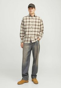 Chemise en flanelle à carreaux avec des tons beige et marron, patte de boutonnage et poche poitrine ; associée à un jean en denim bleu et des bottes beiges.