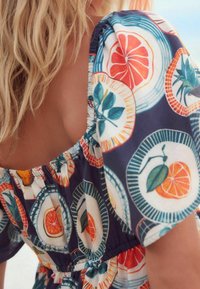 Vestido de tela con estampado floral que presenta vibrantes diseños de frutas cítricas en tonos de azul, naranja y rojo, con escote y mangas elásticas gathered.