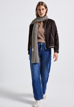 Veste bomber marron, haut beige, jean large bleu, et écharpe grise. Baskets blanches avec des accents beiges. Le tissu semble lisse et confortable.
