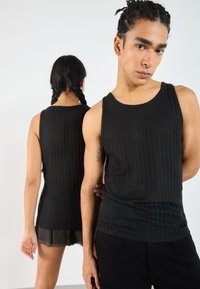 Black ribbed tank tops worn by two figures; one faces forward, other is turned back. Features a crew neckline and regular fit.