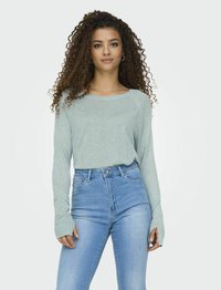 Camisa de manga larga verde claro con cuello redondo, combinada con jeans azules de cintura alta, con una textura suave y un diseño ajustado.