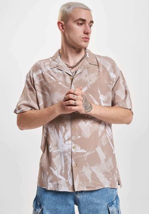 Camicia a maniche corte in tessuto marrone chiaro con motivi astratti bianchi, dotata di colletto e bottoni frontali.
