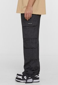 Sorte cargo-bukser med flere lommer, lige pasform og elastiske manchetter. Sammen med sorte og hvide sneakers.