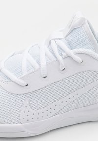 Vita sportskor med överdel i mesh, platta snören, runda hål och en perforerad Nike-logotyp på sidan. Slät sula för bra grepp.