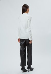 Witte gebreide trui met een hoge halslijn, gecombineerd met zwarte faux leren broek met wijdere pijpen en zwarte puntige hakken. Eenvoudige, strakke lijnen.