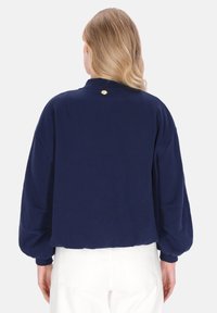 Marineblauwe cropped sweatshirt met lange, opgepofte mouwen en een afgeronde hals, voorzien van een gouden knoopdetail aan de achterkant. Soepele textuur.