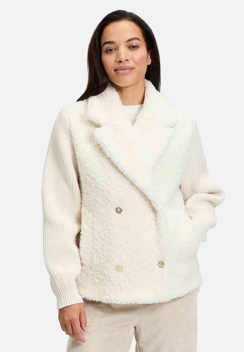Hvid faux fur dobbeltbrystet jakke med store revers, ribbede ærmer og guldfarvede knapper. Glat tekstur og oversized pasform.