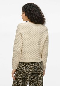 Suéter de punto color crema con un patrón de diamantes texturizado, cuello redondo y puños acanalados, combinado con pantalones de estampado de leopardo.