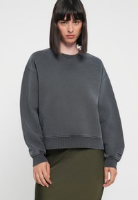 Gray sweatshirt with a textured finish, round neckline, and oversized sleeves. Paired with a dark green skirt for a layered look.