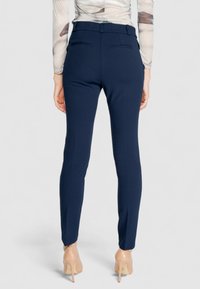 Pantalon navy ajusté avec une texture lisse, doté de passants de ceinture, de deux poches arrière et d'un design de jambes fuselées, associé à des talons beiges.