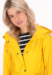 Rumena vodoodporna jakna z vezalko na kapuci, z zadrgo spredaj in z gumbi. Nosi se čez črno-belo prugasto majico, ki ima majhen logotip dežnika.