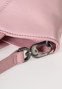 Borsa in pelle rosa con una texture liscia, hardware in metallo scuro a contrasto, una cucitura e un fermaglio in stile moschettone.