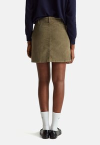 Olivově zelená kordová mini sukně s přímým střihem, předními a zadními kapsami a viditelnými švy, kombinovaná s bílými ponožkami a černými botami.