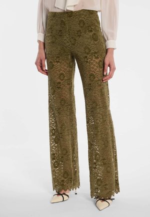 Pantalon large en dentelle florale vert olive porté avec un chemisier blanc et des chaussures pointues crème avec des lanières noires.