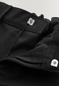 Czarny materiałowy element garderoby z zapięciem na zamek błyskawiczny i metalowymi ozdobami. Materiał o fakturze z wyraźnymi detalami szwów oraz podszewką.