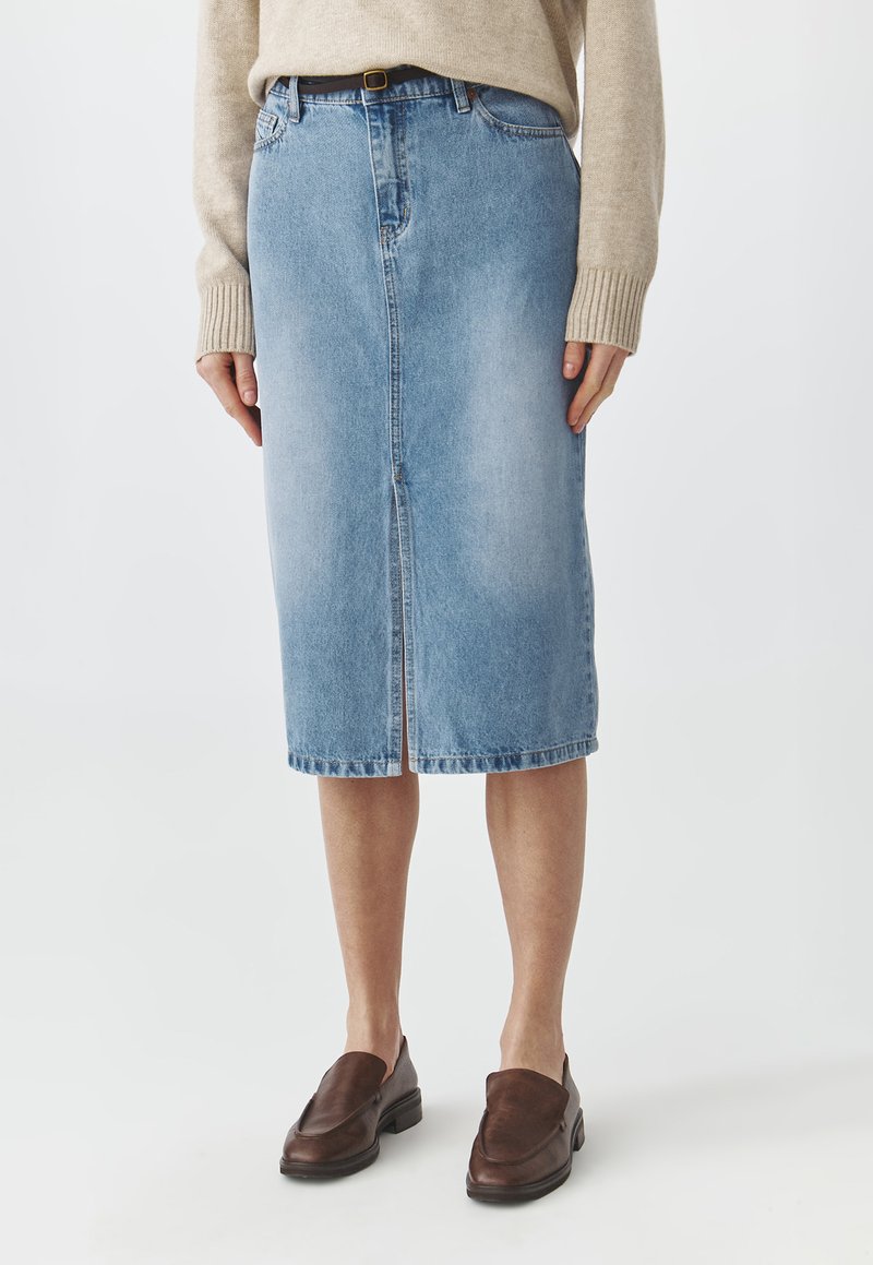 Lichtblauwe denim kokerrok met een voorkieslip en rechte snit. Kenmerkt zich door een hoge taille en riemlussen. G gedragen met bruine instappers.