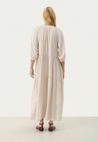 Robe beige à manches longues, à volants, de coupe ample, dotée de manches ballon et d'une texture douce, portée avec des sandales à lanières marron.