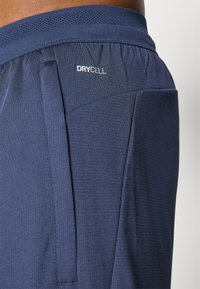 Shorts de sport navy en tissu texturé, avec une taille élastique en mesh, une poche sur le côté et un logo "DRYCELL" à l'arrière.