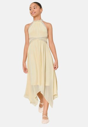 Mädchen, das selbstbewusst in einem ärmellosen, blassgelben Kleid mit Perlenbesatz und asymmetrischem Saum geht, dazu trägt sie rosa Ballettschuhe.