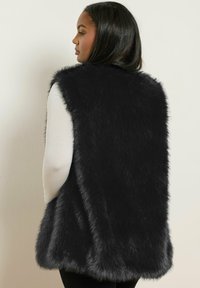 Chaleco de pelo sintético negro con un alto cuello, diseño sin mangas y textura suave. Los bordes son ligeramente redondeados, lo que proporciona una silueta relajada.