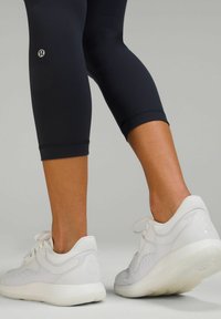 Vita atletiska skor med texturerade detaljer och snörning, parat med figurnära svarta leggings som sträcker sig till halva vaden.