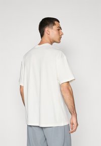 White cotton t-shirt with a crew neck and short sleeves, featuring a relaxed fit and smooth texture, viewed from the back.