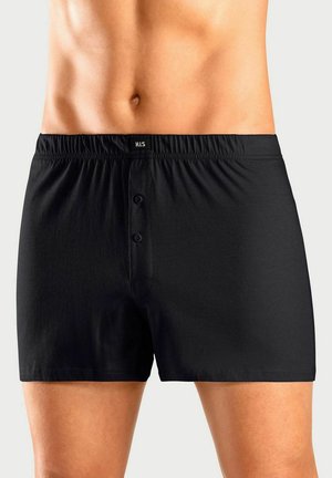 Nahaufnahme eines männlichen Oberkörpers, der schwarze Boxershorts mit elastischem Bund, einem zweiknöpfigen Hosenschlitz und dem "H.I.S"-Label trägt.