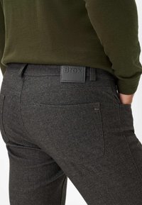 Grijze, gestructureerde broeken met een slim-fit ontwerp, voorzien van een leren logo-embleem op de taille en subtiele stikdetails op de zakken.