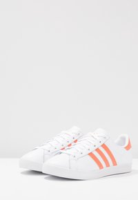 Vita sneakers med tre korallfärgade ränder, gummisula, rund tå och snörningsdesign. Tillverkade av slätt syntetmaterial.