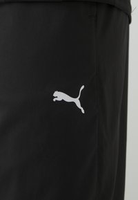 Juodi sportiniai šortai, pagaminti iš lengvos medžiagos, su balta Puma logotipo etikete kairėje pusėje. Lygus paviršius su elastingu juosmeniu.
