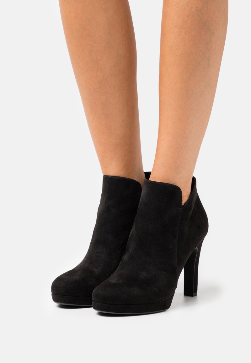 Schwarze Wildleder-Stiefeletten mit glatter Textur, runder Zehenform und hohem Absatz. Ausschnittbereiche am Knöchel sorgen für dezente Details.