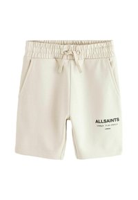 Lys beige bomuldsbukser med elastisk talje, snørre, sidelommer og et trykt logo i sort på fronten.