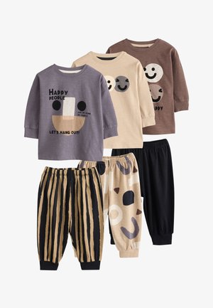 Tre completi per bambini con maglie a manica lunga e pantaloni con vita elastica in tonalità neutre, con grafiche di faccine sorridenti e motivi astratti.