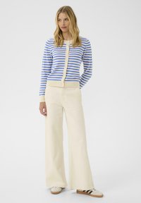 Striped cardigan in blue and white with a cream hem, buttoned front, paired with wide-leg, light beige pants and beige sneakers.