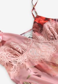 Camisolă roz din satin cu model floral și detalii intricate din dantelă de-a lungul bustului, cu bretele subțiri pe un fundal alb.